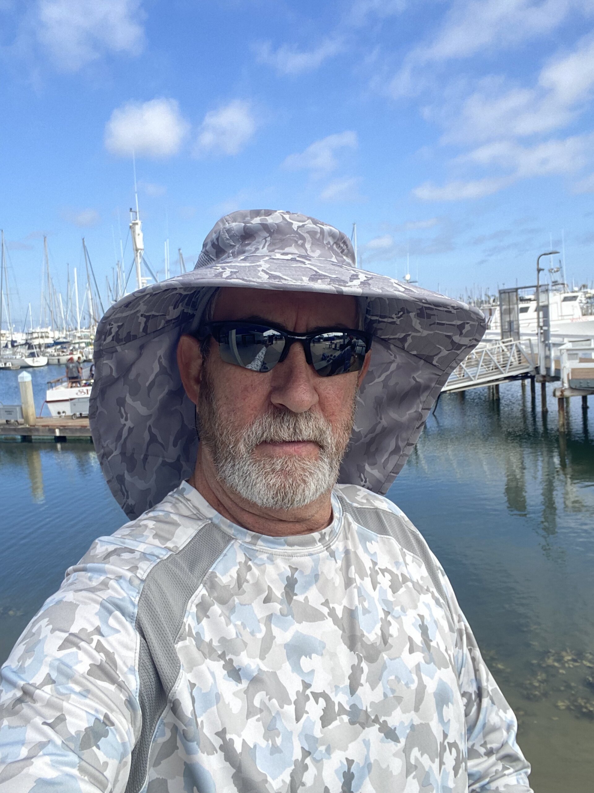 Man with sunglasses and hat looking into camera, marina in the background